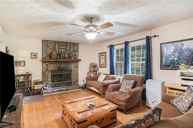 living room with ceiling fan, a stone fireplace, hardwood / wood-style floors, and a textured ceiling