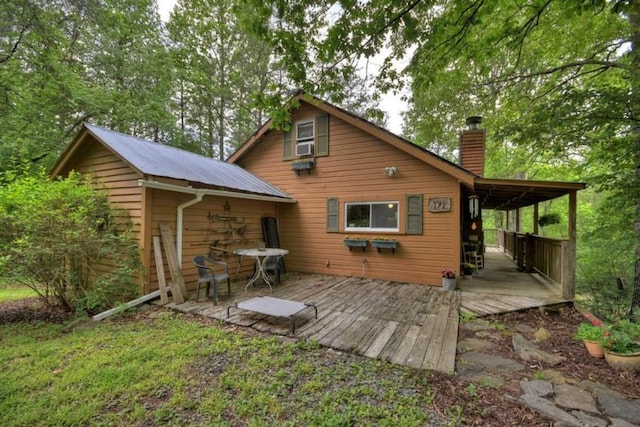 back of house featuring a chimney, a deck, and metal roof
