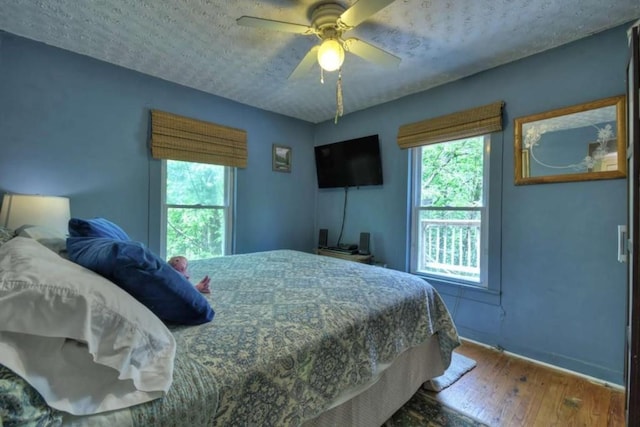 bedroom featuring hardwood / wood-style floors, baseboards, a textured ceiling, and a ceiling fan