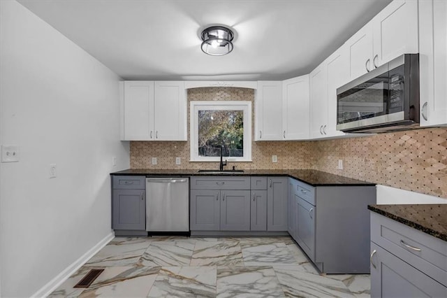 kitchen featuring appliances with stainless steel finishes, white cabinetry, dark stone counters, and sink