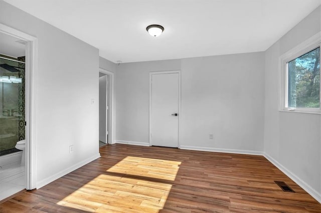 unfurnished bedroom featuring ensuite bath, a closet, and wood-type flooring