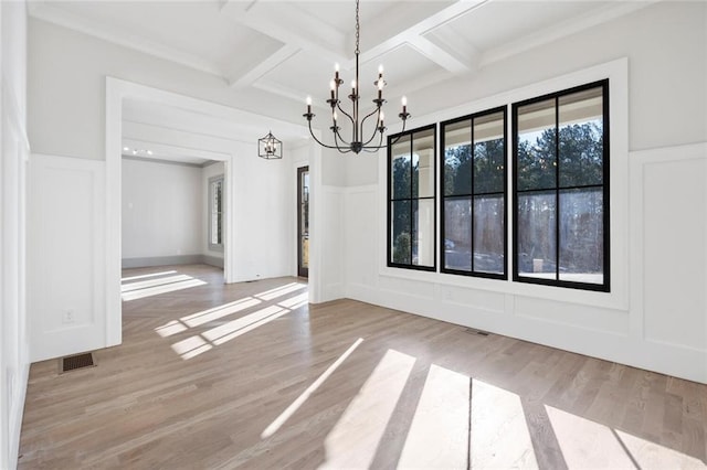 unfurnished dining area with beam ceiling, coffered ceiling, a chandelier, and light wood-type flooring