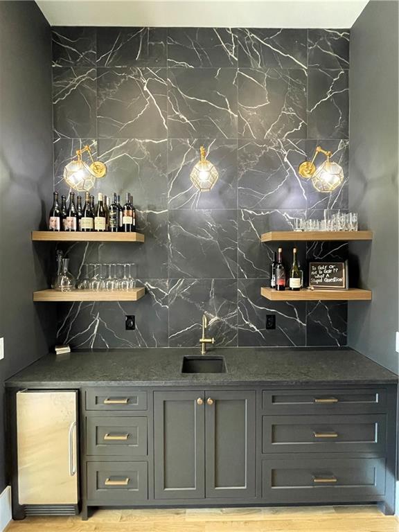 bar with fridge, light hardwood / wood-style floors, sink, and backsplash