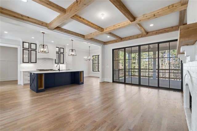 kitchen with beamed ceiling, hanging light fixtures, a large island with sink, a notable chandelier, and light hardwood / wood-style flooring