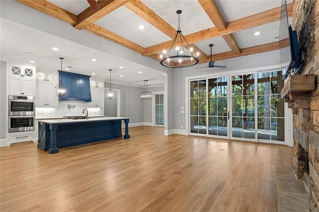 living room with ceiling fan with notable chandelier, a fireplace, sink, light hardwood / wood-style floors, and beam ceiling