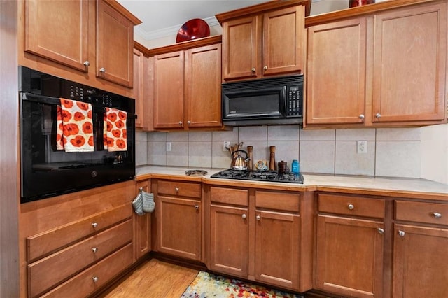 kitchen with decorative backsplash, light wood-type flooring, ornamental molding, and black appliances