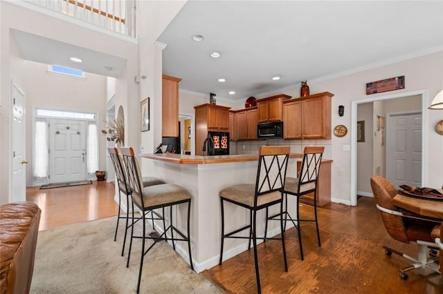 kitchen featuring kitchen peninsula, wood-type flooring, crown molding, and black appliances