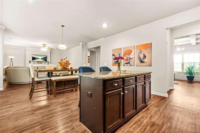 kitchen with light stone counters, baseboards, dark brown cabinetry, wood finished floors, and hanging light fixtures