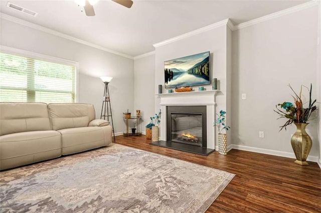living room with ceiling fan, visible vents, baseboards, ornamental molding, and wood finished floors