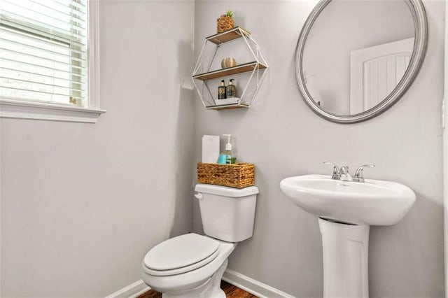 half bath with baseboards, toilet, and a sink