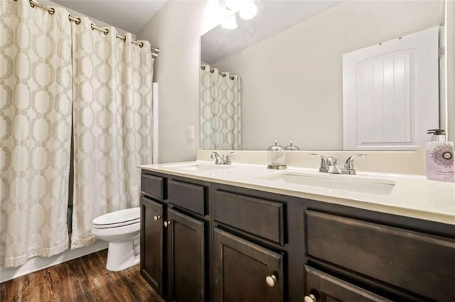 bathroom with toilet, double vanity, a sink, and wood finished floors