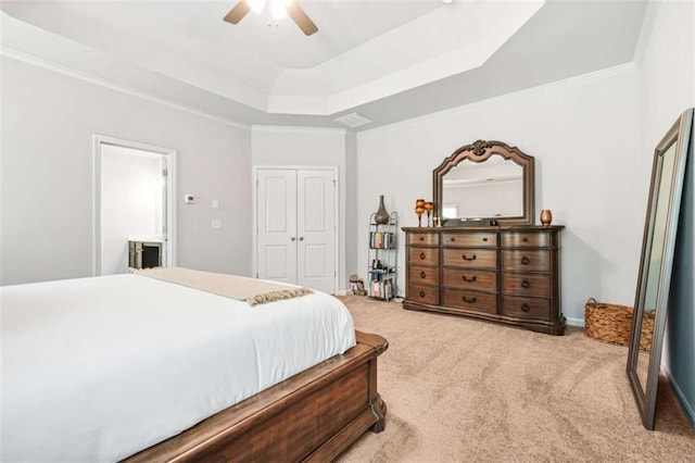 bedroom featuring crown molding, a tray ceiling, a closet, light carpet, and a ceiling fan