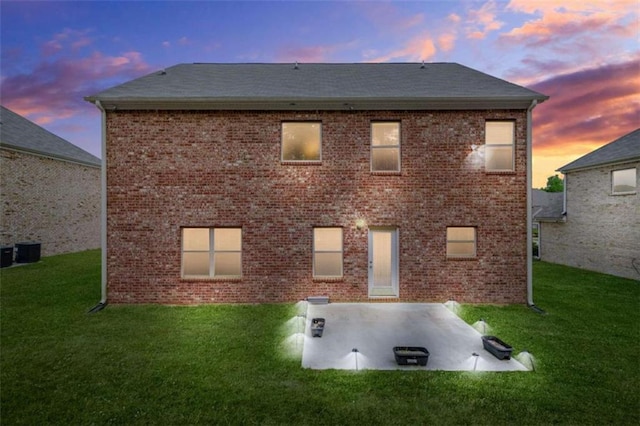 back of property at dusk with a lawn, a patio area, and brick siding