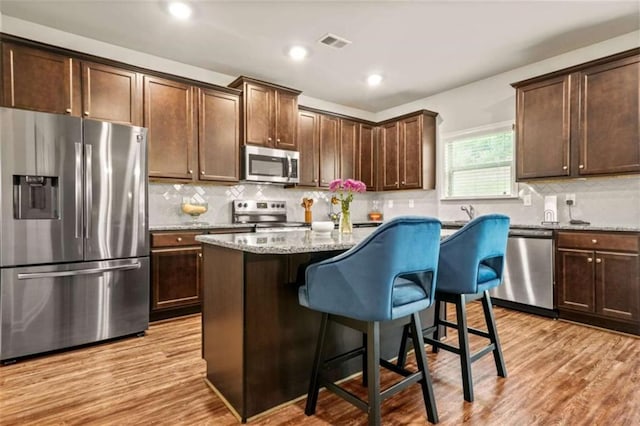 kitchen featuring decorative backsplash, visible vents, stainless steel appliances, a kitchen bar, and light stone countertops