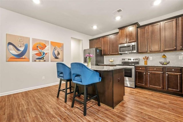 kitchen with a breakfast bar area, tasteful backsplash, visible vents, stainless steel appliances, and a kitchen island