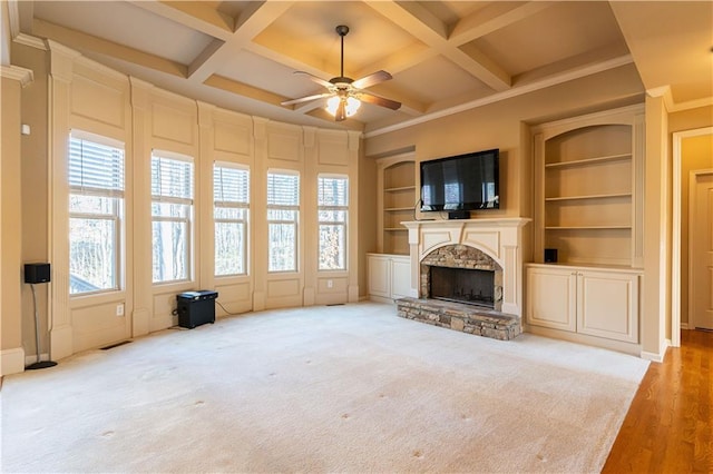 unfurnished living room featuring coffered ceiling, built in shelves, beamed ceiling, and a stone fireplace