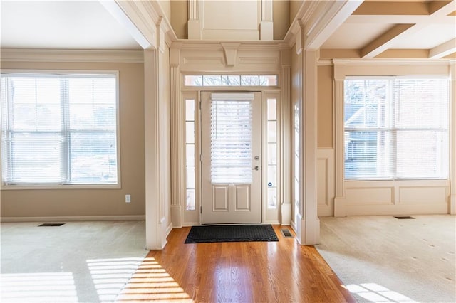 carpeted foyer entrance with ornamental molding, beamed ceiling, and plenty of natural light