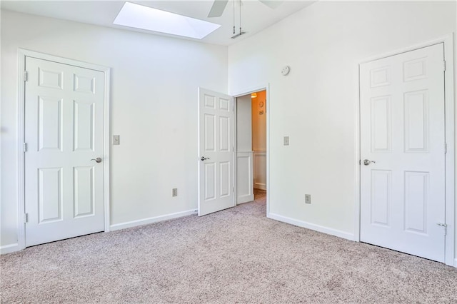 unfurnished bedroom featuring vaulted ceiling with skylight, light colored carpet, and ceiling fan