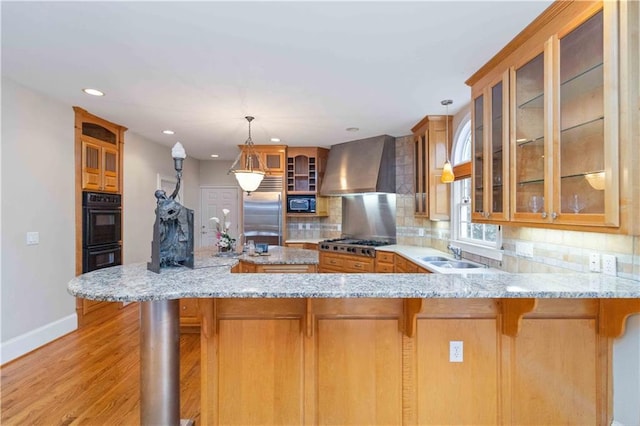 kitchen featuring wall chimney exhaust hood, black appliances, pendant lighting, and kitchen peninsula