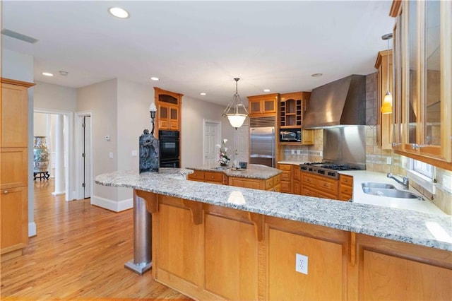 kitchen featuring kitchen peninsula, wall chimney exhaust hood, sink, a kitchen island, and black appliances