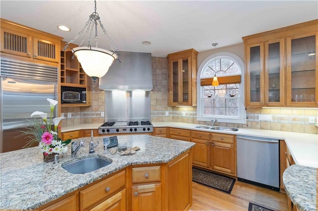 kitchen with appliances with stainless steel finishes, wall chimney exhaust hood, sink, backsplash, and decorative light fixtures