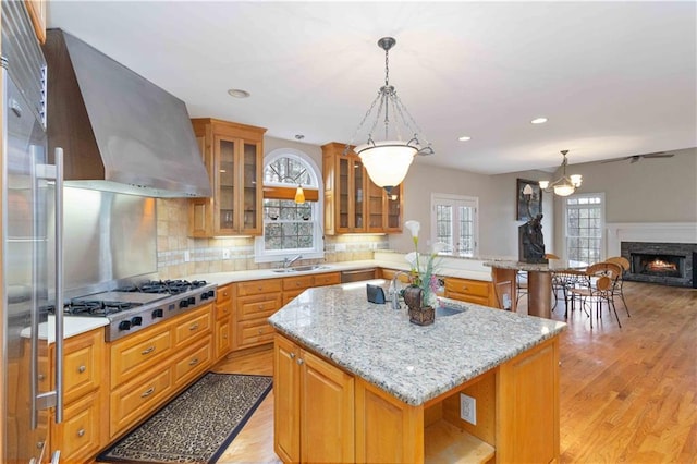 kitchen featuring wall chimney exhaust hood, sink, backsplash, a kitchen island, and stainless steel appliances