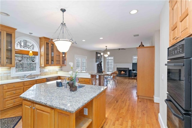 kitchen with light wood-type flooring, a kitchen island, sink, backsplash, and light stone counters