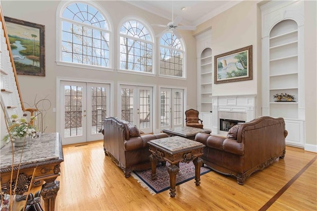 living room featuring ceiling fan, french doors, built in features, ornamental molding, and light hardwood / wood-style floors