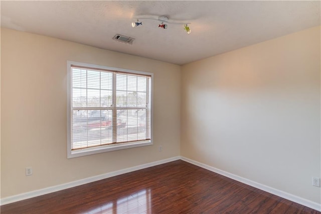 unfurnished room with dark wood-style flooring, visible vents, and baseboards