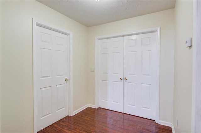 unfurnished bedroom with a closet, dark wood finished floors, a textured ceiling, and baseboards