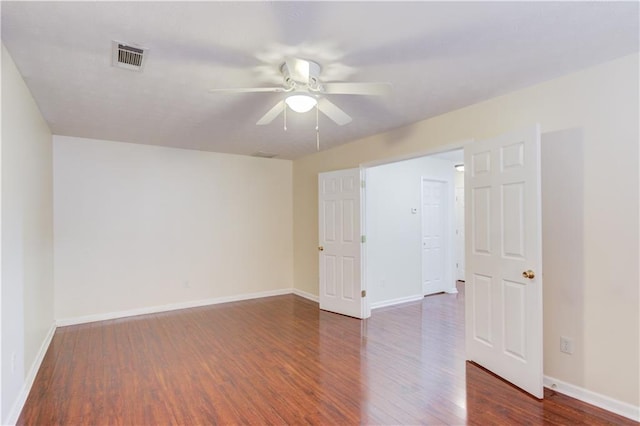 empty room featuring a ceiling fan, dark wood finished floors, visible vents, and baseboards