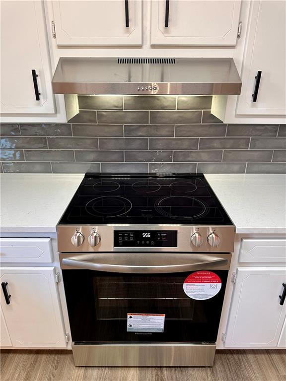 kitchen featuring white cabinets, wall chimney exhaust hood, decorative backsplash, and stainless steel stove