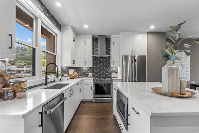 kitchen featuring decorative backsplash, appliances with stainless steel finishes, wall chimney exhaust hood, sink, and white cabinetry