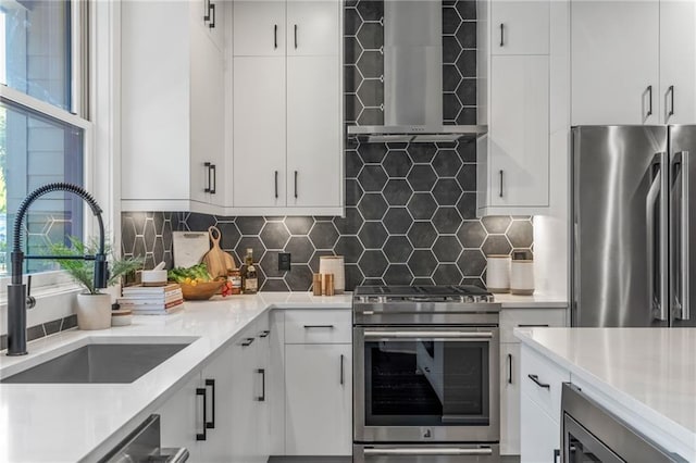 kitchen featuring backsplash, white cabinets, wall chimney range hood, sink, and premium appliances