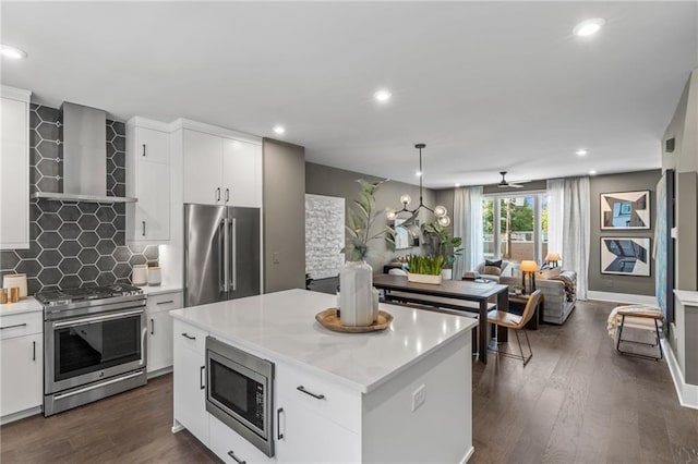 kitchen with pendant lighting, a center island, wall chimney range hood, appliances with stainless steel finishes, and white cabinetry