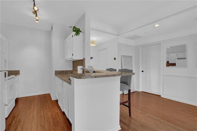 kitchen featuring white cabinetry, light hardwood / wood-style flooring, a kitchen breakfast bar, and kitchen peninsula