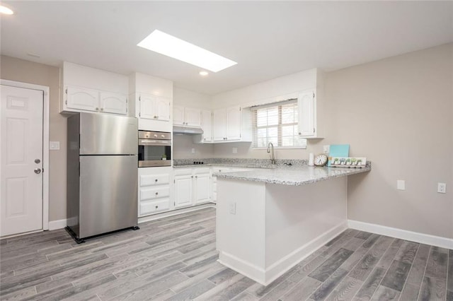 kitchen featuring under cabinet range hood, a peninsula, white cabinets, stainless steel appliances, and a sink