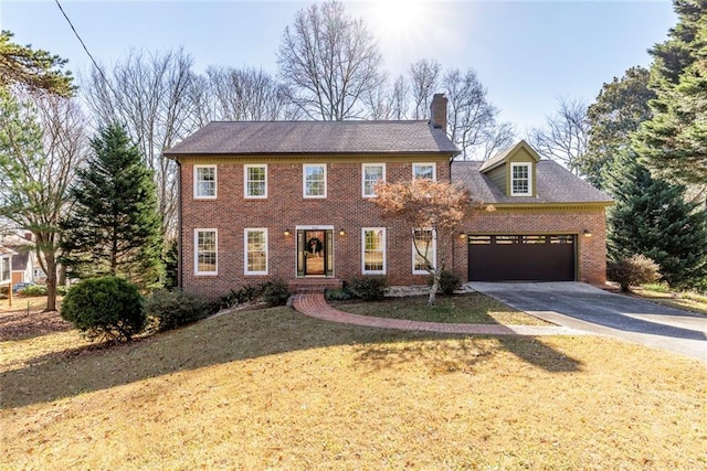 colonial-style house featuring an attached garage, brick siding, concrete driveway, a chimney, and a front yard