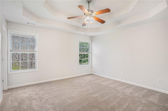carpeted empty room featuring baseboards, ceiling fan, visible vents, and a raised ceiling