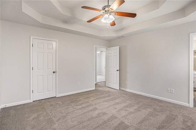 unfurnished bedroom featuring a tray ceiling, baseboards, visible vents, and carpet flooring