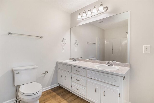 bathroom featuring double vanity, a sink, toilet, and wood finished floors