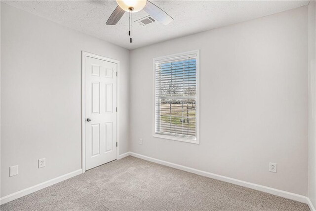 carpeted empty room with a textured ceiling, baseboards, ceiling fan, and visible vents