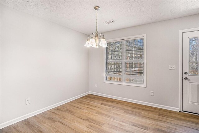 unfurnished dining area featuring baseboards, visible vents, light wood-style floors, and a chandelier