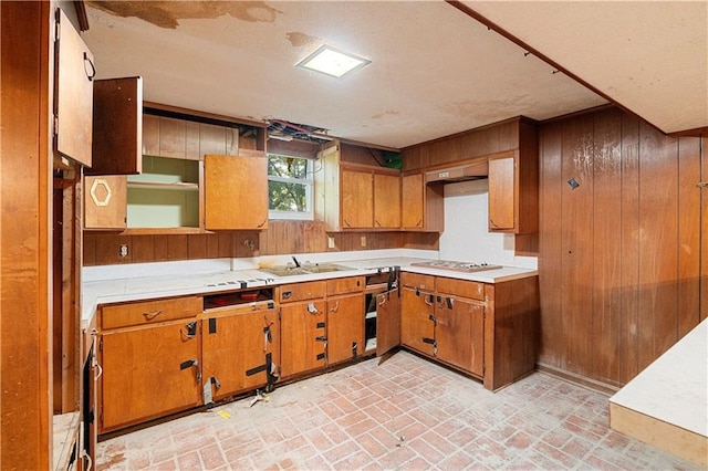 300 S Dale Ave, Calhoun, GA 30701 - kitchen with brick patterned flooring, wooden walls, brown cabinetry, light countertops, and stainless steel gas cooktop