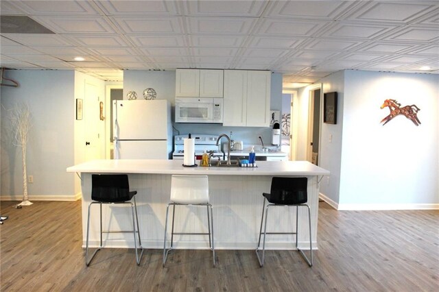 kitchen featuring a breakfast bar, wood-type flooring, white appliances, and white cabinetry