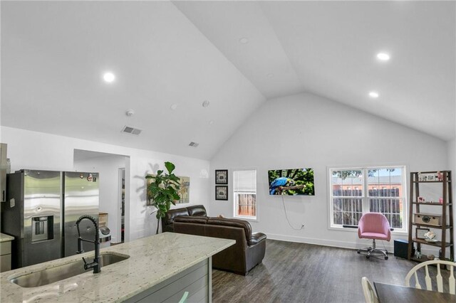 kitchen featuring high vaulted ceiling, light stone countertops, dark wood-type flooring, sink, and stainless steel fridge with ice dispenser