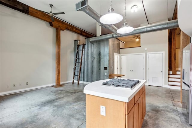 kitchen with ceiling fan, a kitchen island, stainless steel gas cooktop, baseboards, and concrete floors