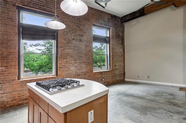 kitchen featuring decorative light fixtures, brick wall, concrete floors, and stainless steel gas stovetop