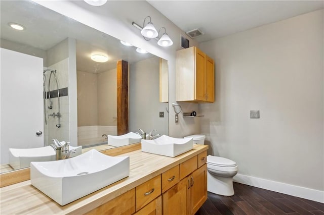 bathroom featuring double vanity, wood finished floors, a sink, baseboards, and tiled shower