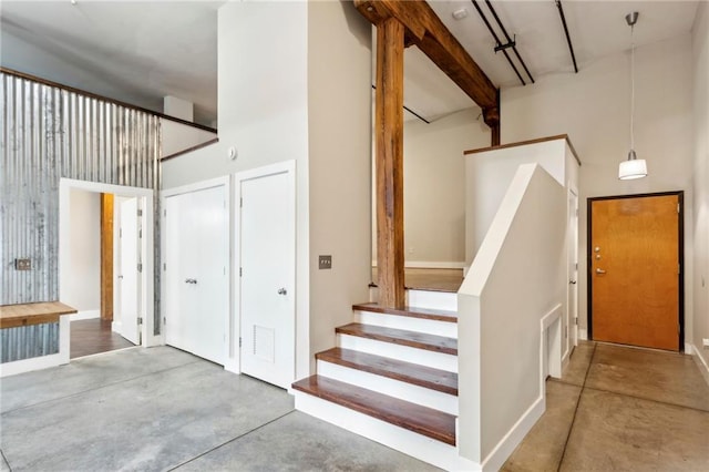 stairway featuring beamed ceiling, finished concrete floors, and a towering ceiling